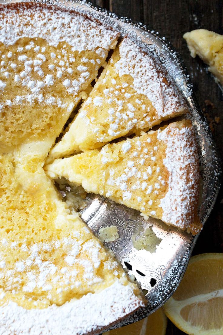 a lemon cake with powdered sugar on top is cut into slices and sits next to sliced lemons