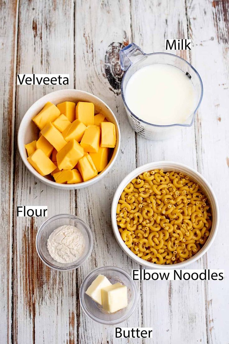 ingredients to make macaroni and cheese are shown in bowls on a white wooden table