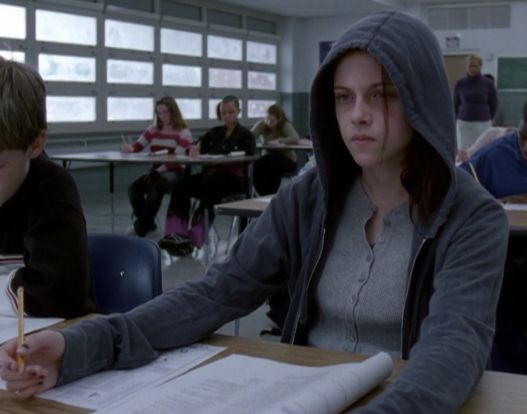 two students sitting at desks in a classroom with one writing on paper and the other holding a pencil