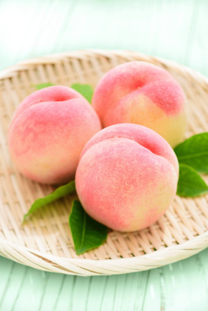 three fresh peaches with green leaves on a wicker plate