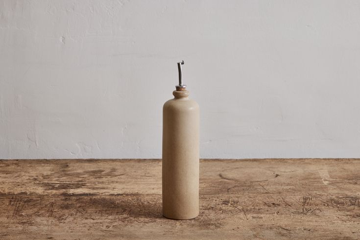 an empty bottle on a wooden table with a hook in it's top and a white wall behind it