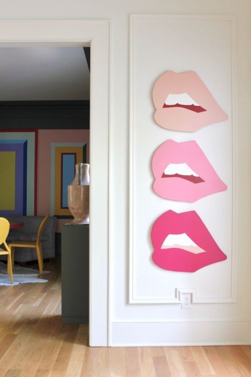 three pink lips are hanging on the wall next to a yellow chair in front of a white door