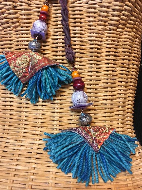 a woven necklace with beads and tassels hanging from it's side on a wicker basket