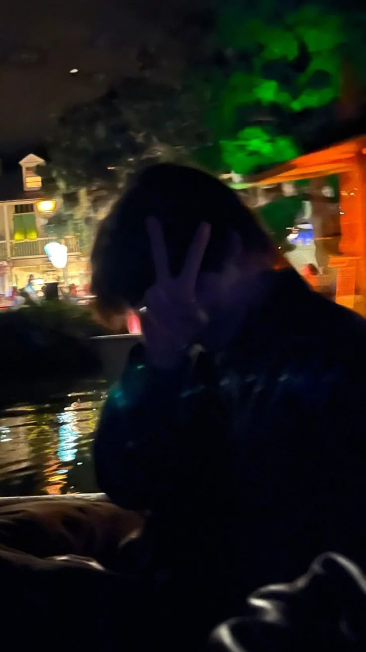 a man sitting in front of a river at night talking on a cell phone while holding his hand up to his face