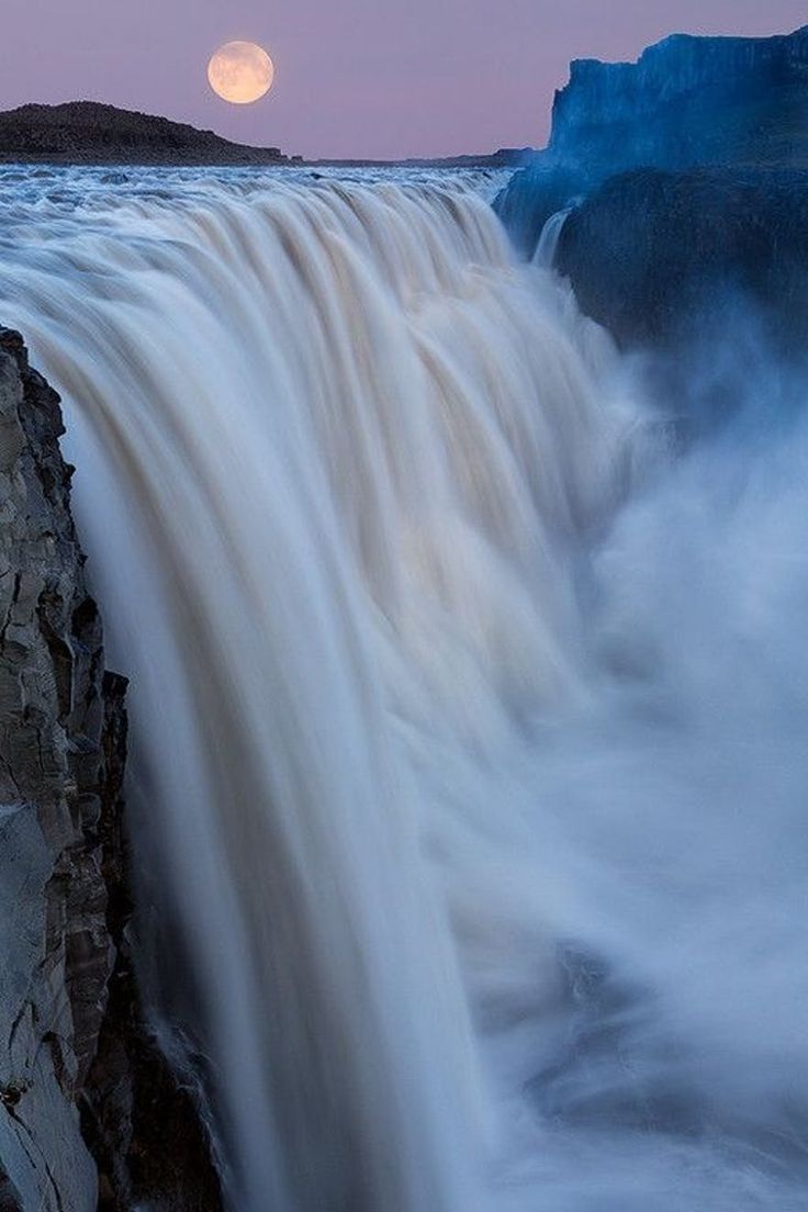 the moon is setting over an icy waterfall