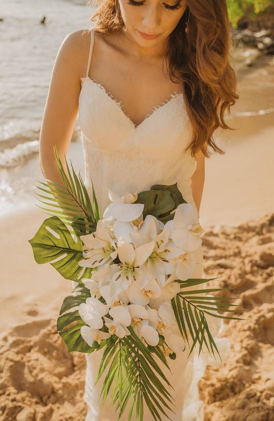 a woman in a wedding dress holding a bouquet on the beach