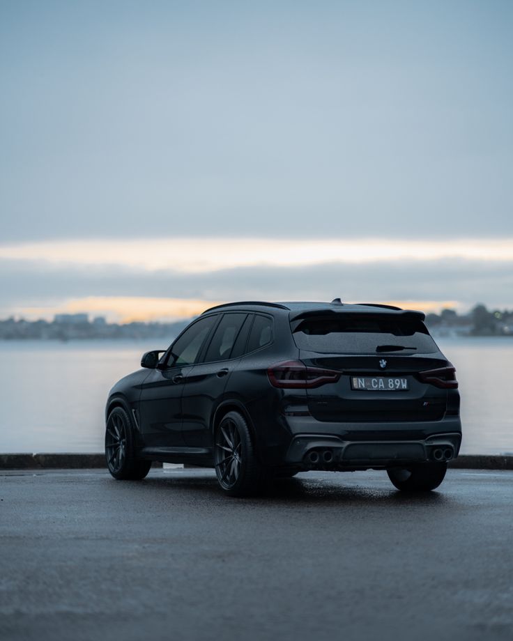 a black bmw suv parked on the side of a road next to a body of water