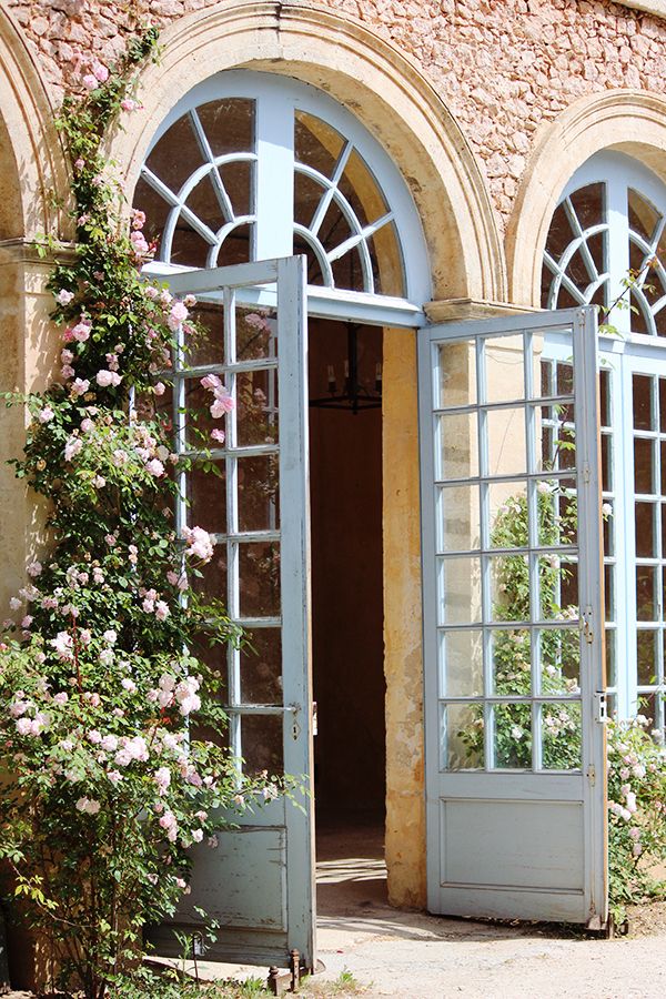 an open door to a building with flowers growing out of the window sills