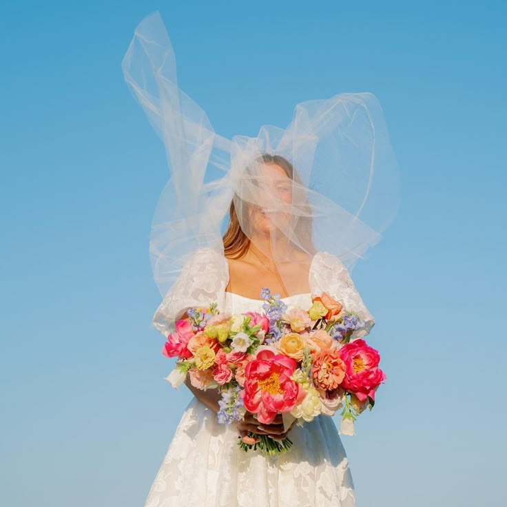 a woman in a wedding dress holding a bouquet of flowers with veil over her head