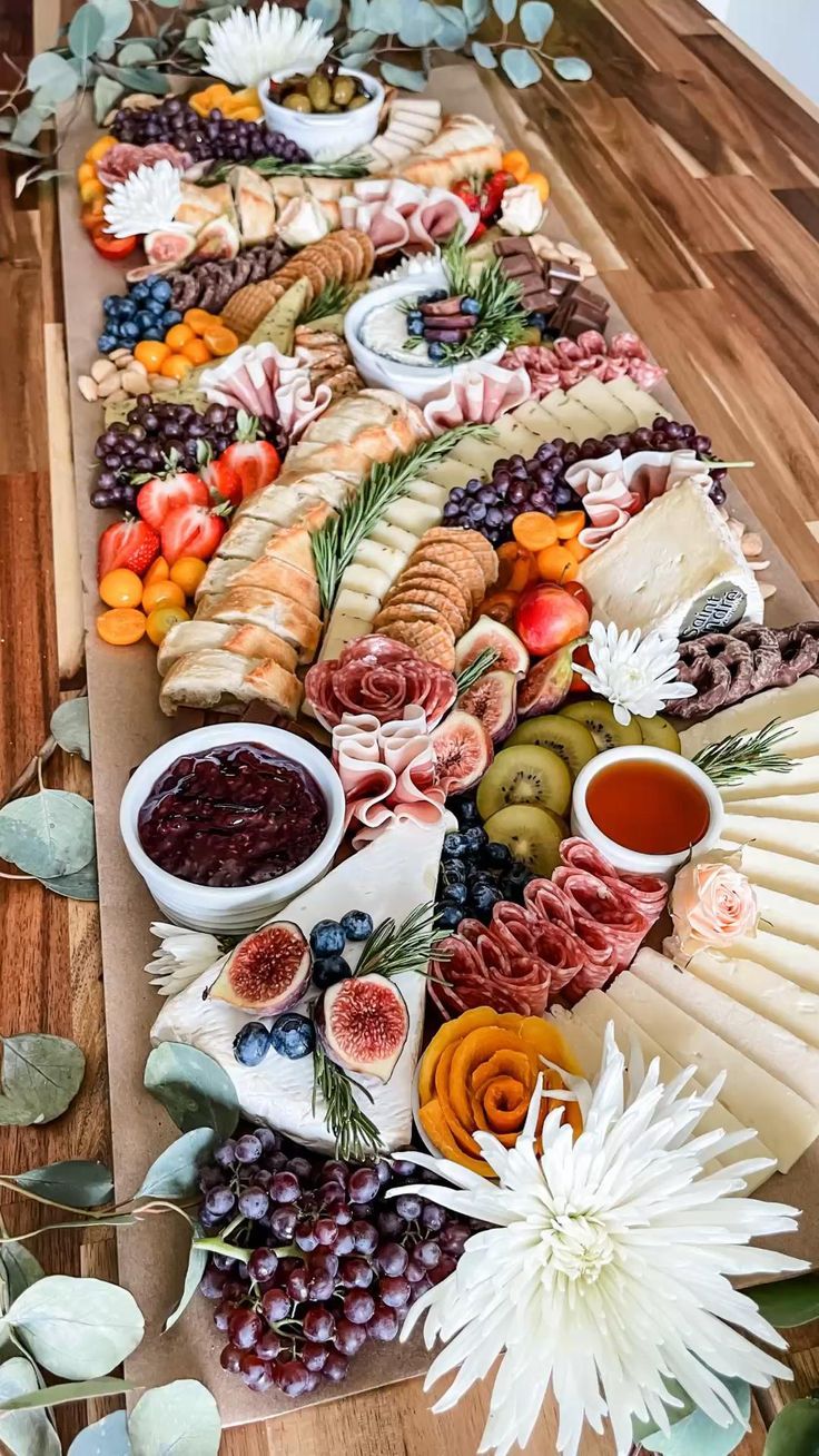 an assortment of food is laid out on a long table with leaves and flowers around it