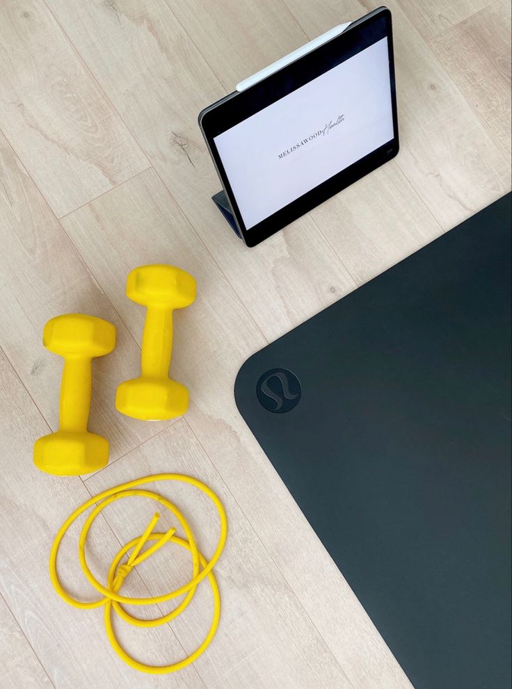 a laptop computer sitting on top of a wooden floor next to two yellow dumbs