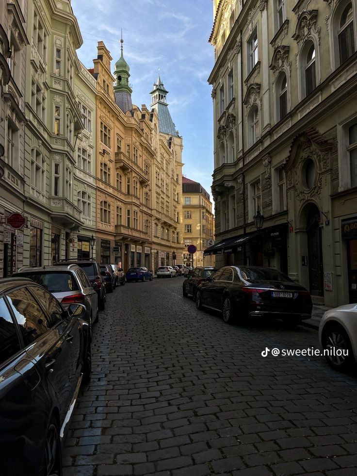 cars parked on the side of a street next to tall buildings with steeple tops