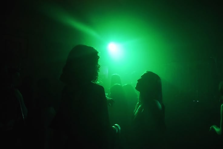 two people standing in front of a green light at a party or disco with their backs turned to the camera