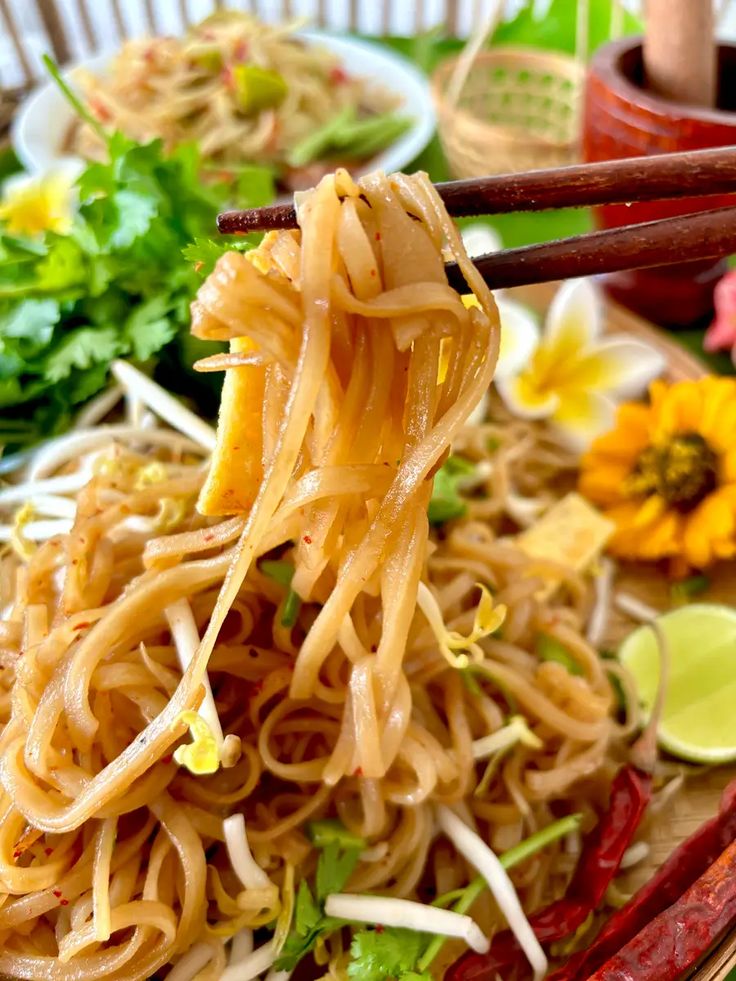 chopsticks holding up noodles with vegetables and sauce on the plate next to it