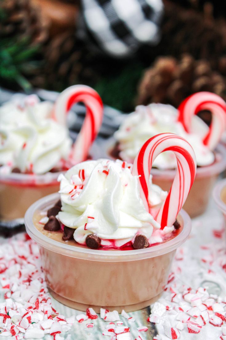 two cups filled with hot chocolate and candy canes on top of a white table cloth