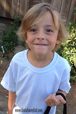 a young boy is holding a black bag and smiling at the camera while standing in front of a wooden fence