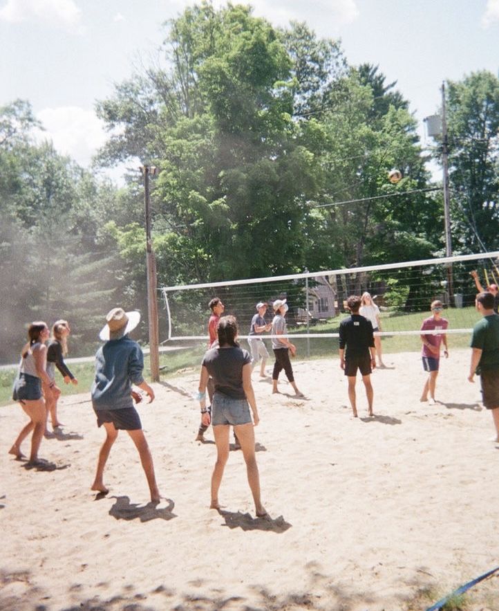 a group of people playing volleyball on a sandy court with trees in the back ground