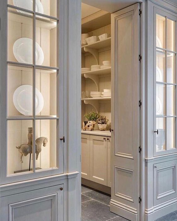 an open door leading to a kitchen with white dishes on the shelves and cupboards