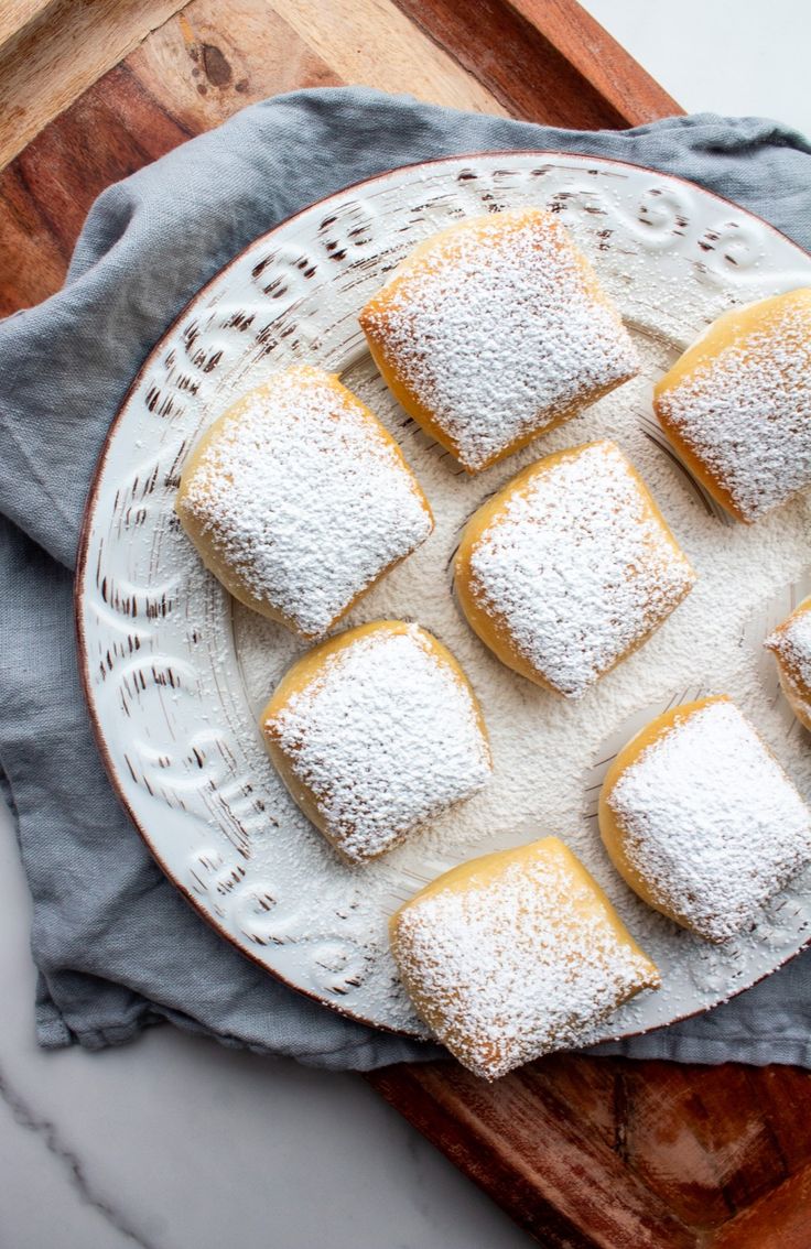 powdered sugar covered pastries on a white plate with blue napkin and wooden cutting board