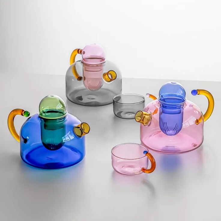 several different colored glass teapots and cups on a table with one cup in the middle