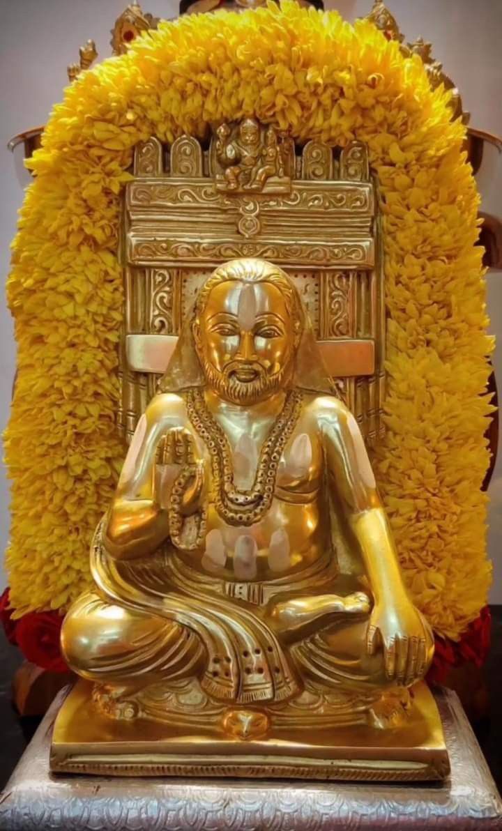 a golden buddha statue sitting in front of a yellow flower covered wall with red and white flowers