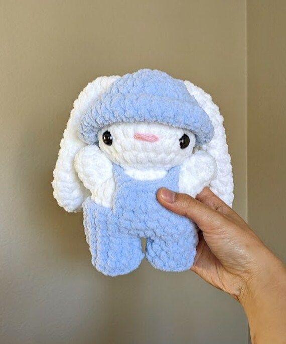 a hand holding a blue and white crocheted stuffed animal in front of a wall