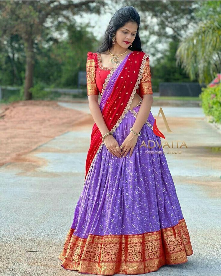 a woman in a purple and red lehenga standing on the street with her hand on her hip