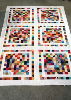 a quilt made out of different colored squares on top of a carpeted floor next to a table