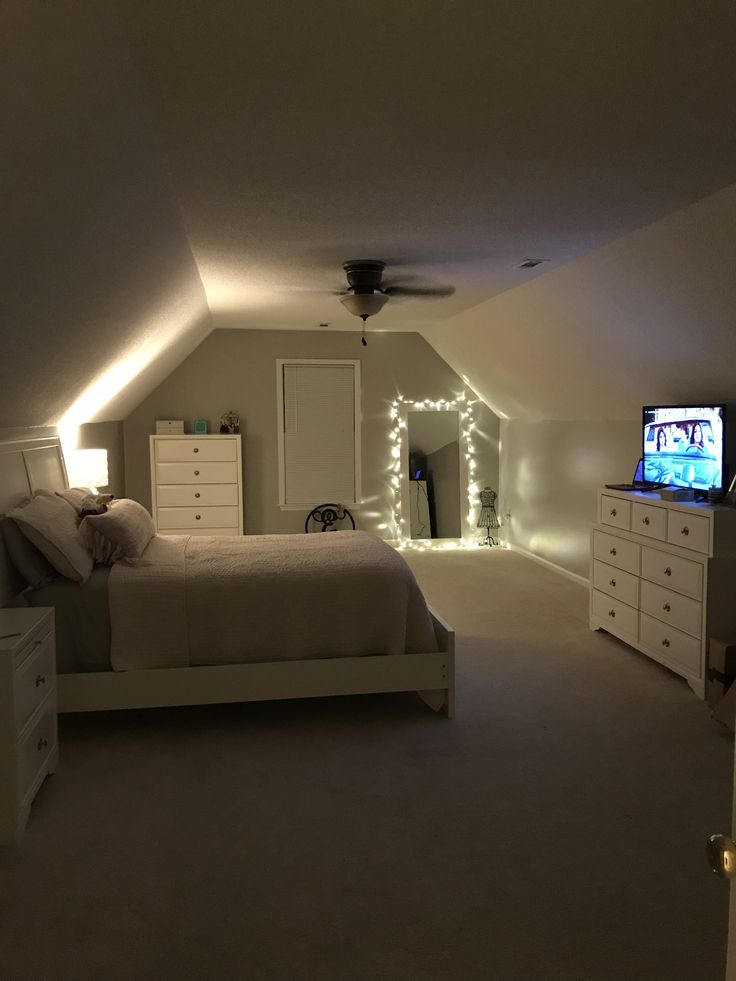 a bedroom with a bed, dressers and television in the corner is lit up by white lights