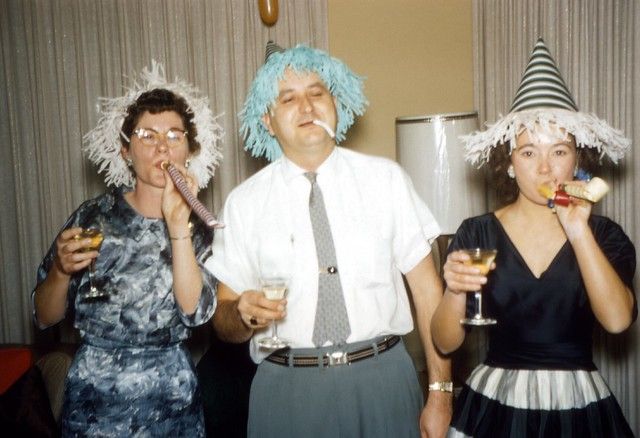 three people in party hats and dress clothes posing for the camera with drinks in their hands