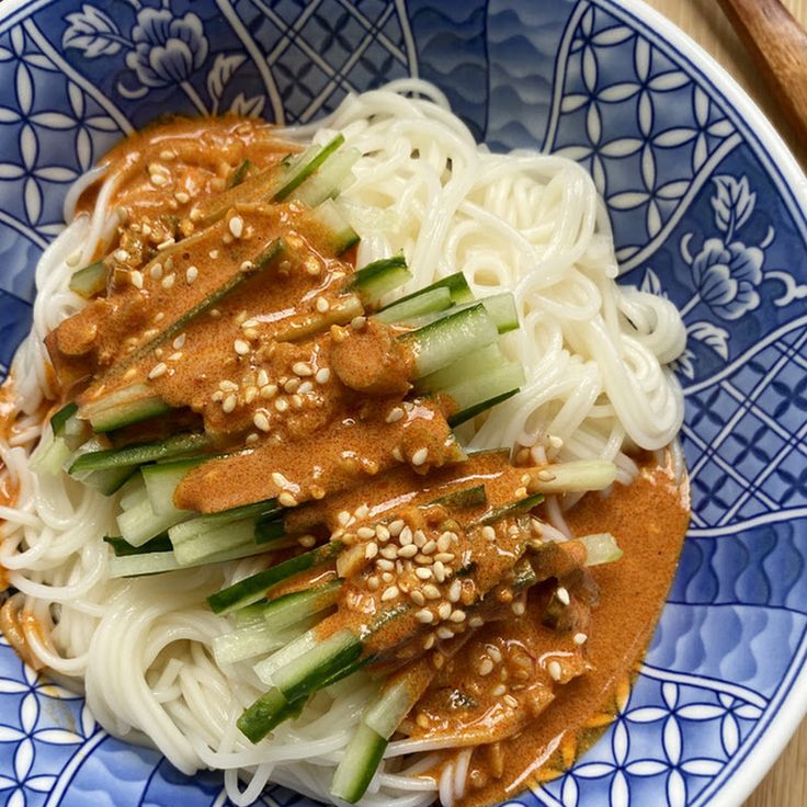 a blue and white plate topped with noodles, sauce and veggies next to chopsticks