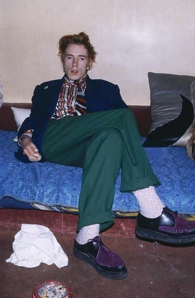 a man sitting on top of a bed next to a blue blanket and pillows with his feet up