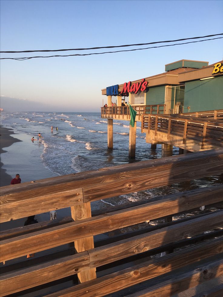 a wooden bench sitting next to the ocean near a pier with people swimming in the water