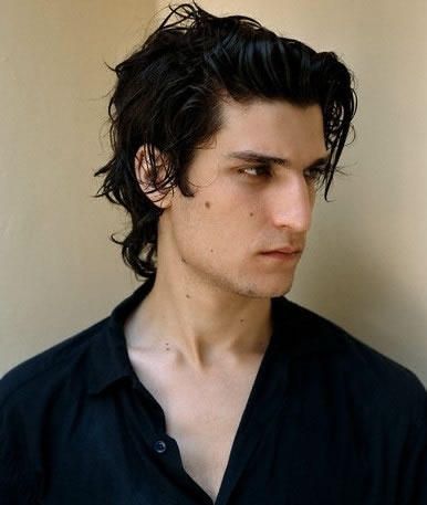 a young man with long hair wearing a black shirt and looking off to the side