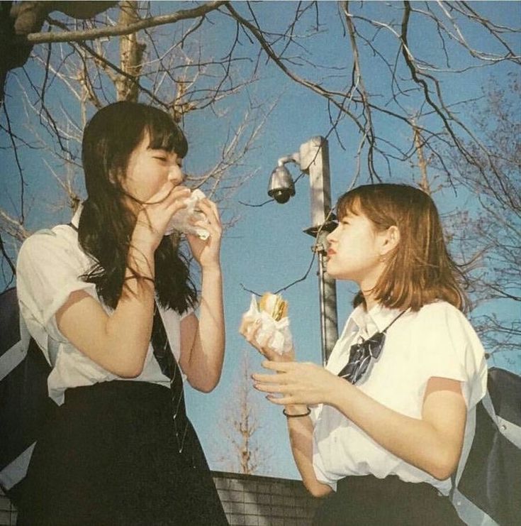 two young women are eating ice cream outside