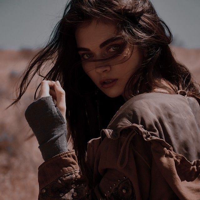 a woman with long hair and glasses posing for a photo in front of a desert background