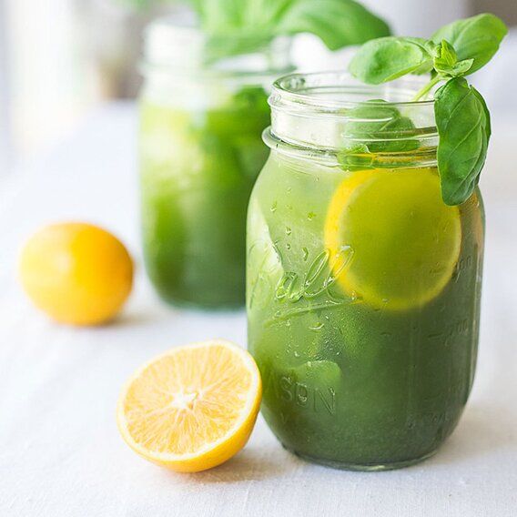 two mason jars filled with green lemonade and minty water next to sliced lemons