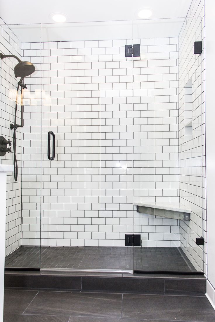 a walk in shower sitting next to a white tiled wall and black tile flooring