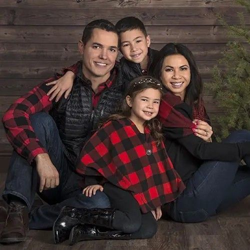 a family posing for a photo in front of a wooden wall with christmas tree and presents