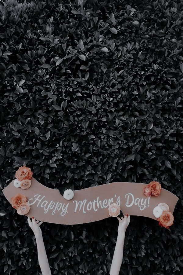 two hands holding a sign that says happy mother's day with flowers on it