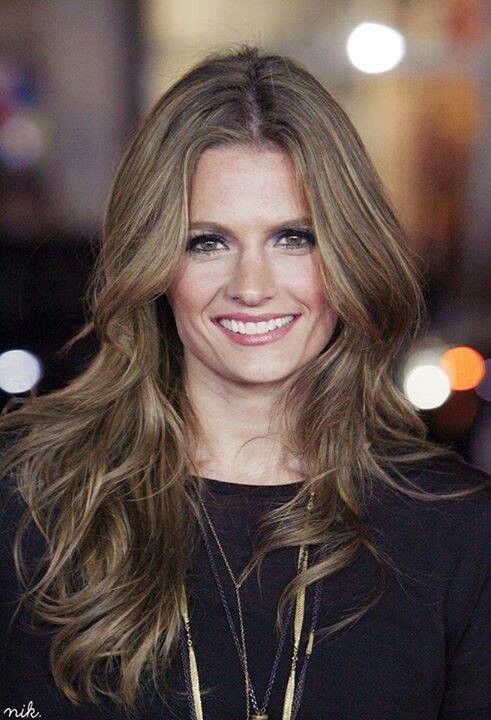 a woman with long hair smiling and wearing a black shirt on the street at night