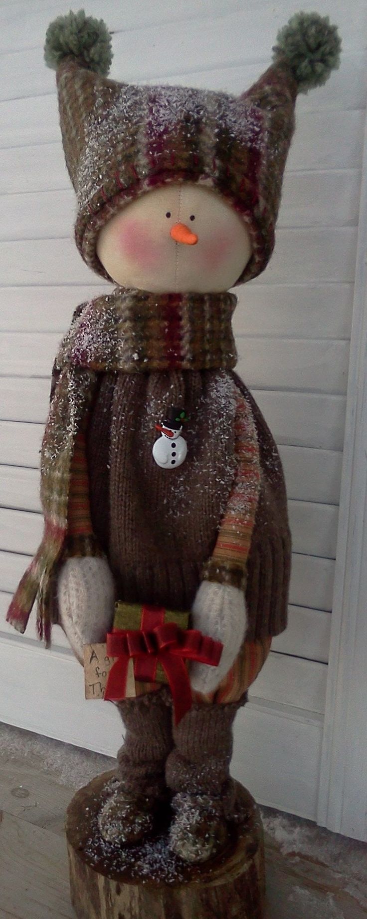 a snowman is sitting on top of a tree stump wearing a knitted hat and scarf