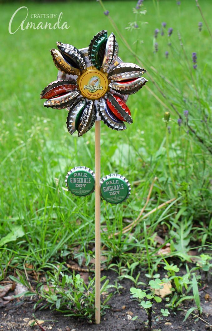 a flower made out of bottle caps sitting on top of a wooden stick in the grass