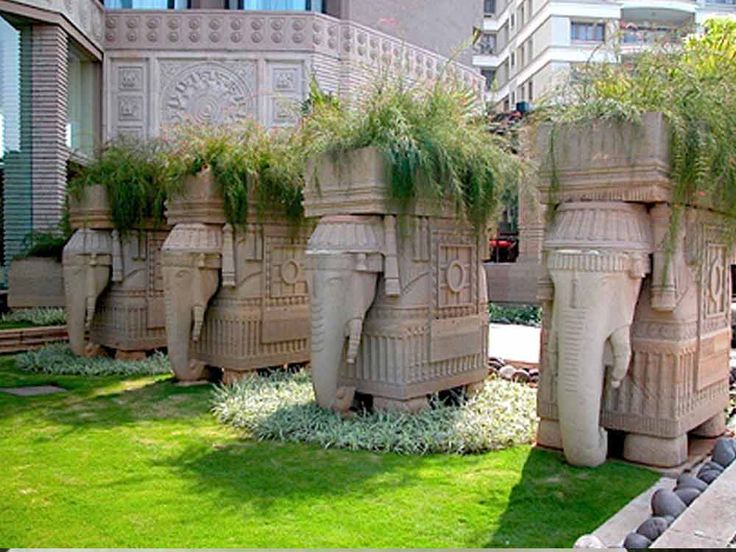 some very big pretty planters in the middle of a grass area with plants growing out of them