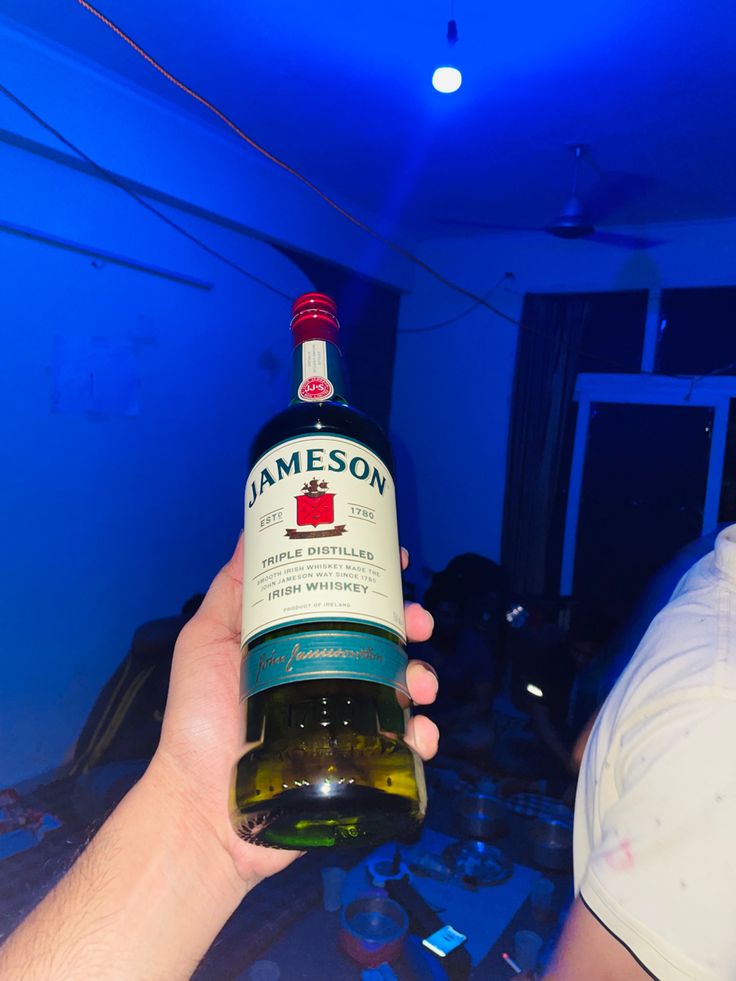 a person holding a bottle of jameson in their left hand, with the light on behind them