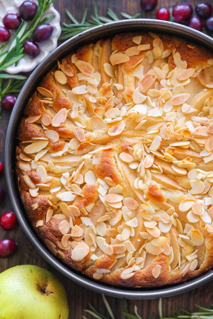 an apple pie with almonds and cranberries on the table next to it