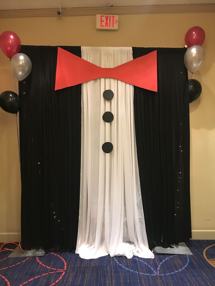 a black and white drapes with red bow tie, balloons and streamers on the floor