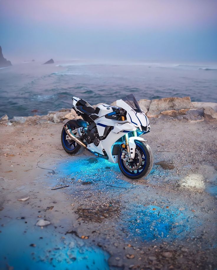 a white and blue motorcycle parked on top of a rocky beach next to the ocean