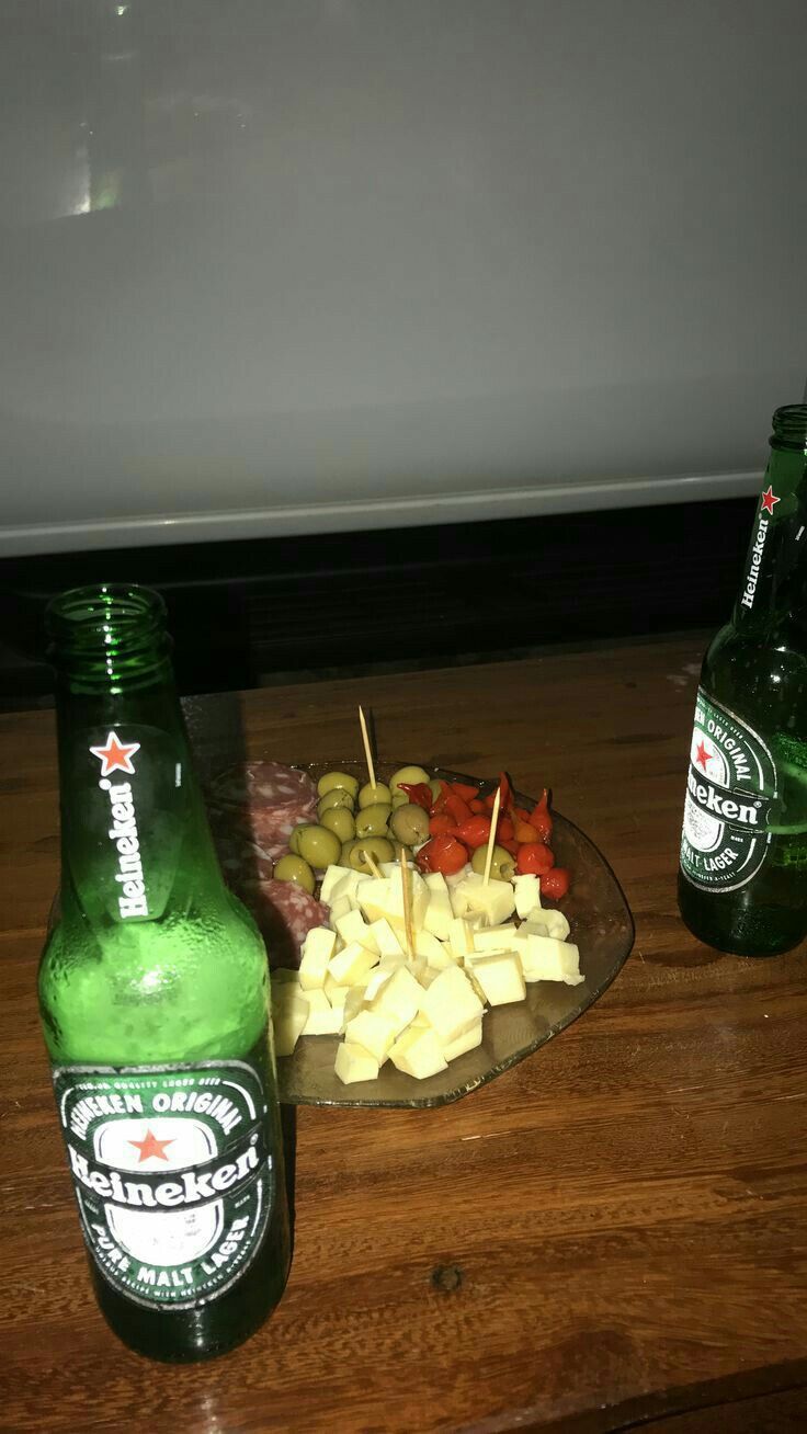 two beer bottles sitting on top of a wooden table next to a platter of food