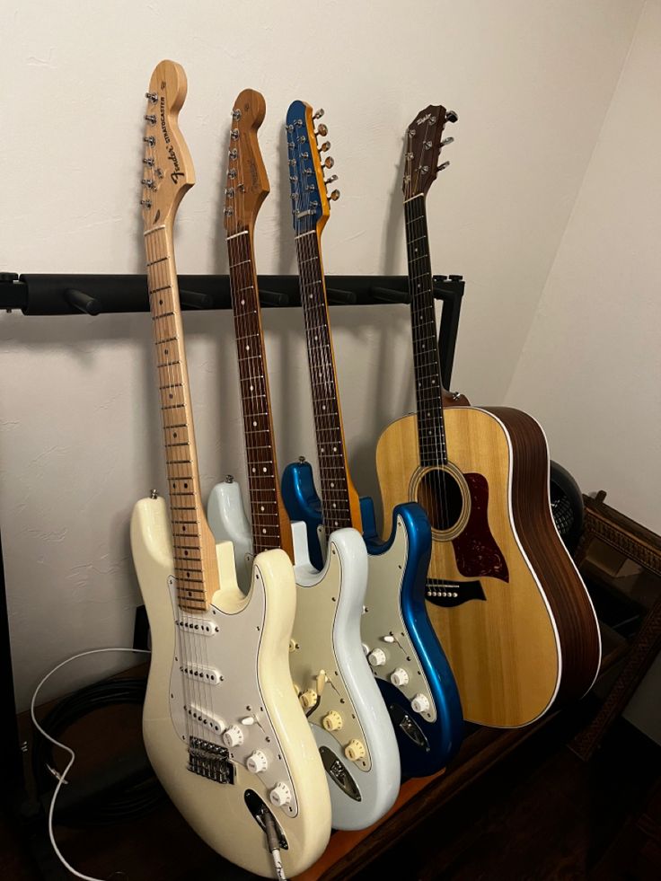 four guitars are lined up in a row on a shelf next to a wall mounted guitar rack